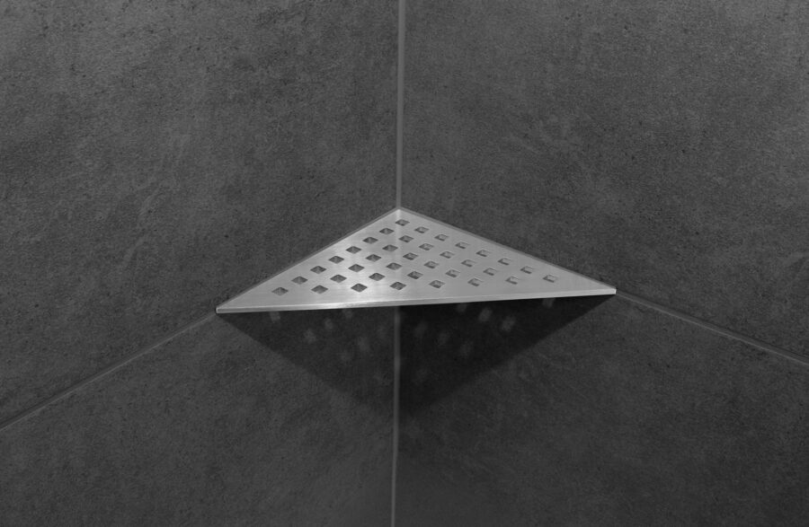 Dreieckige Design-Duschablage aus Edelstahl mit quadratischen Ablauflöchern in einer Duschecke
